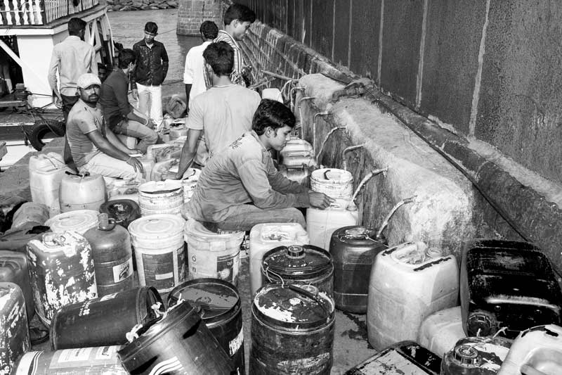 Queued up containers being filled turn-by-turn by boatmen at a public standpoint on the waterfront at Mumbai Harbor, Maharashtra